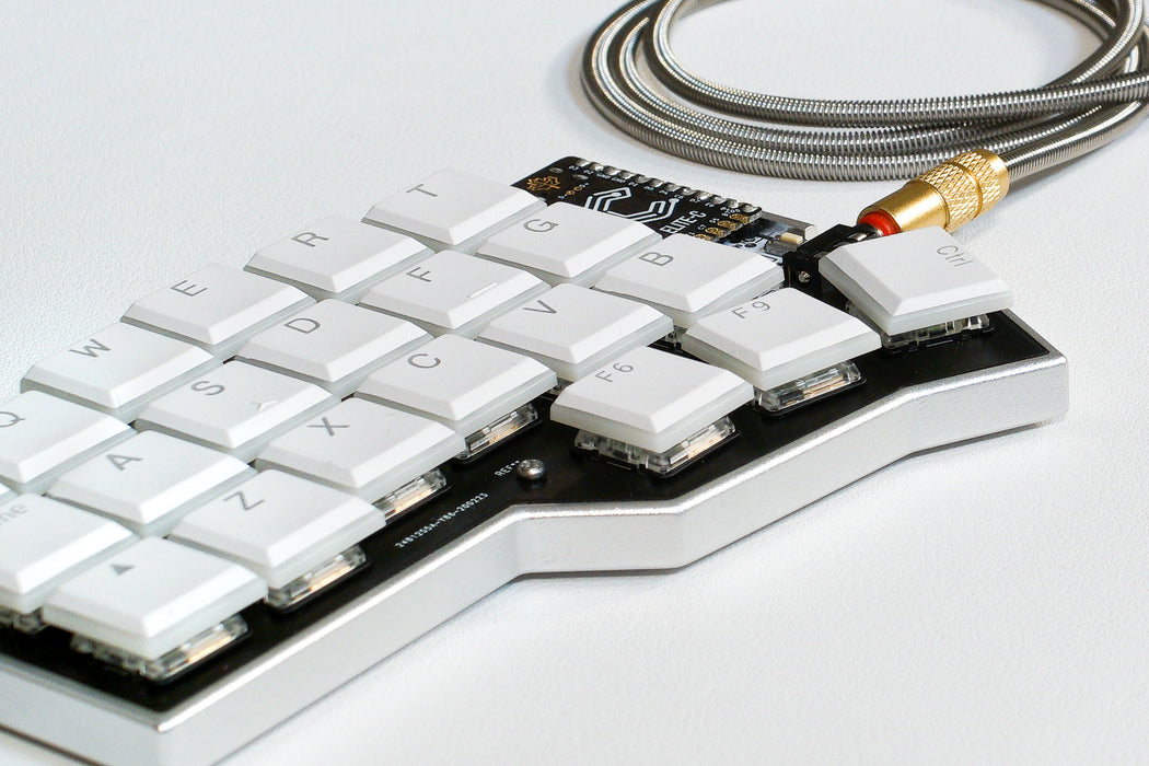 A view of the Corne LP case from the front, showing the aluminium case, white keycaps, Elite C and a metal TRRS cable.